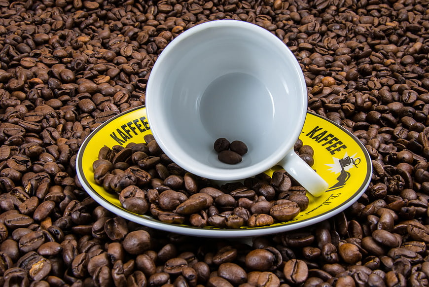 White Coffee Cup on Yellow Saucer Surrounded by Roasted Beans