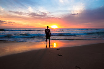 Man Silhouette Watching Sunset on Beach with Footprints