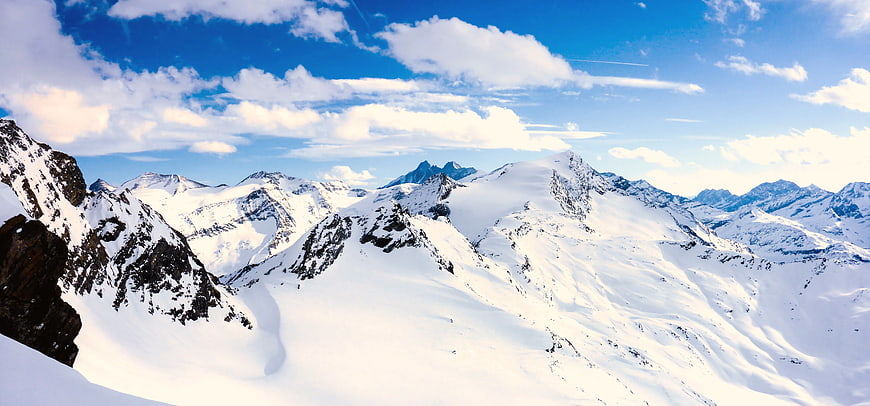 Panoramic View of Snow-Covered Mountain Peaks Under Blue Sky