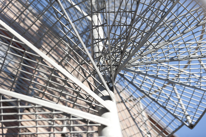 Low angle view of white metal spiral staircase against blue sky