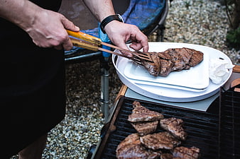 Hands grilling beef steaks on outdoor barbecue