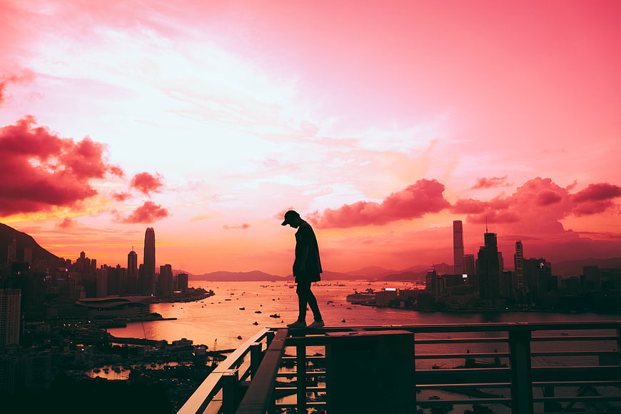 Silhouette of Man Standing on Balcony Overlooking City Skyline at Sunset