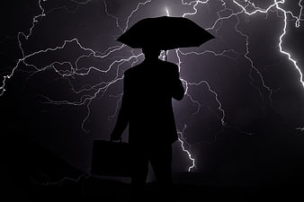 Silhouette of businessman with umbrella against lightning storm