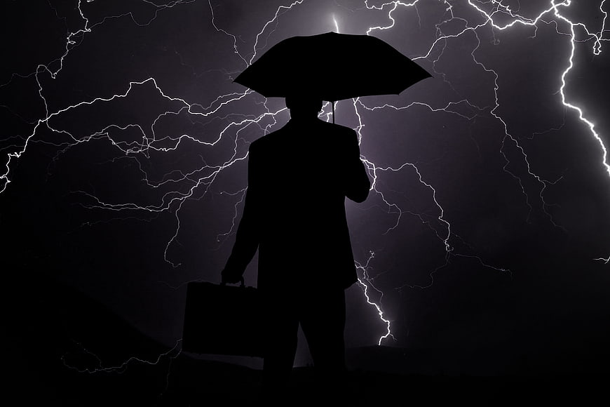 Silhouette of businessman with umbrella against lightning storm