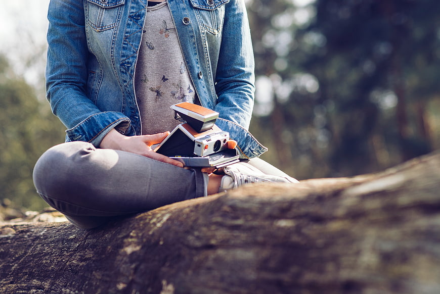 Woman Sitting on Log with Vintage Polaroid Camera