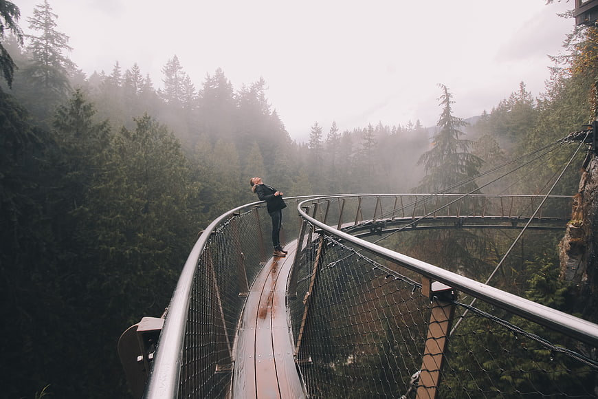 Woman standing on curved suspension bridge in foggy forest