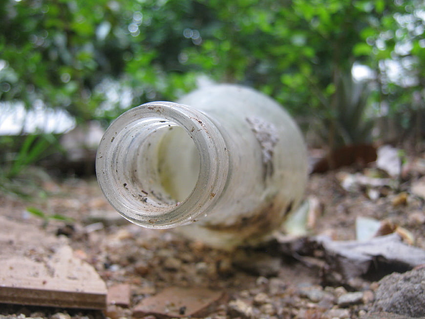 Dirty glass bottle lying on ground in nature