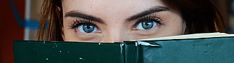 Close-up of Woman's Blue Eyes Peeking Over Green Book