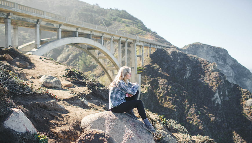 Woman sitting on rock overlooking Bixby Creek Bridge