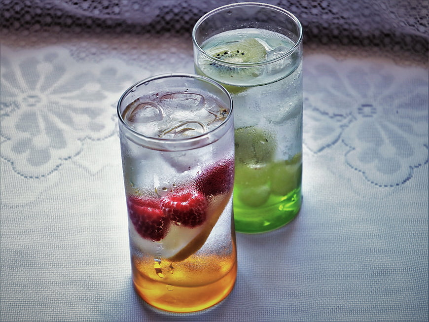 Two glasses of iced fruit-infused water with raspberries and kiwi on a table