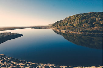 Serene coastal river mouth with sandy banks and grassy dunes