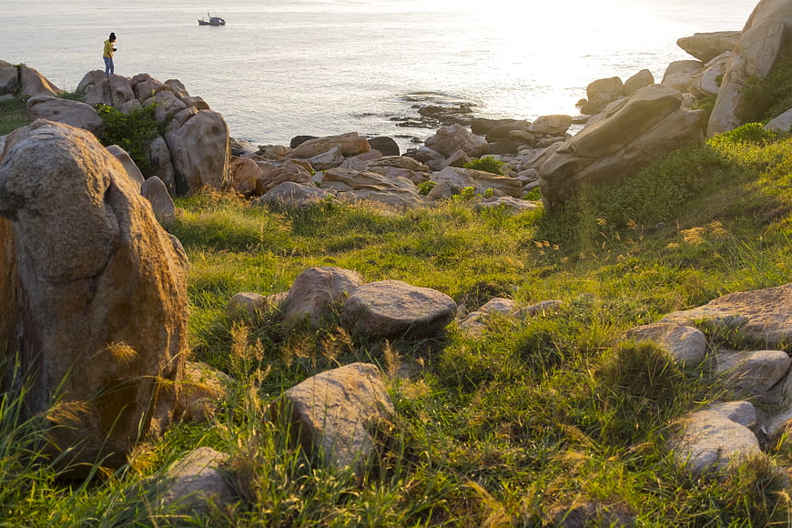 Lone figure standing on rocky coastal landscape at sunset