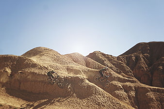 Mountain bikers riding on dusty desert hills under blue sky