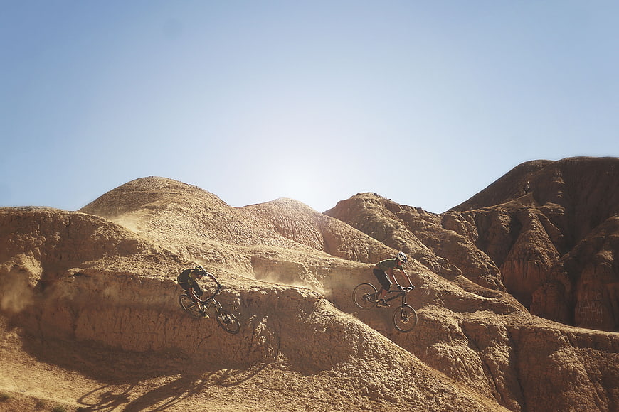 Mountain bikers riding on dusty desert hills under blue sky