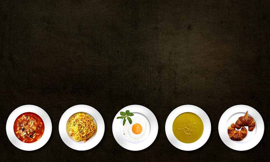 Top View of Five White Plates with Various Dishes on Dark Background