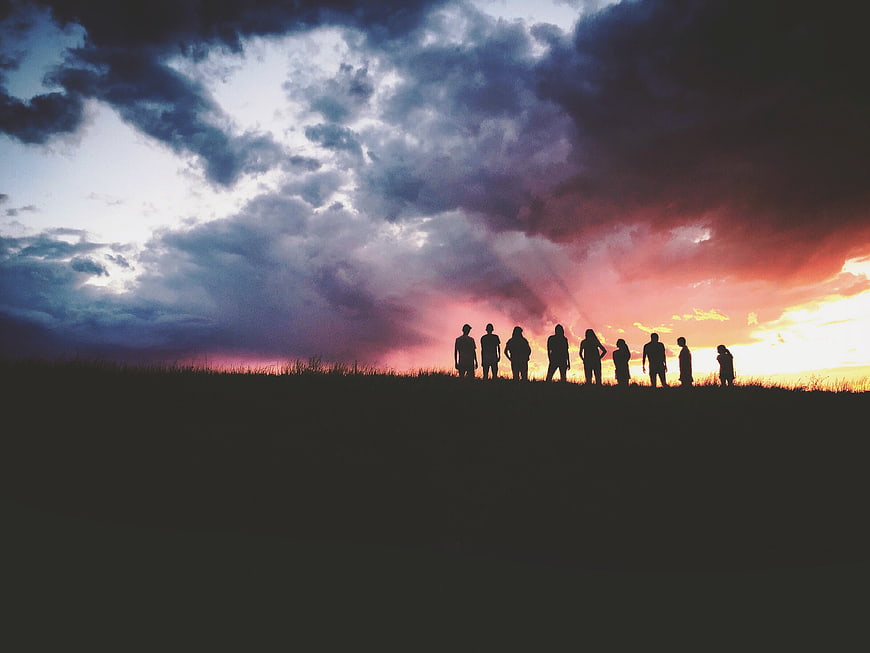 Silhouette of group of friends standing on hill at sunset