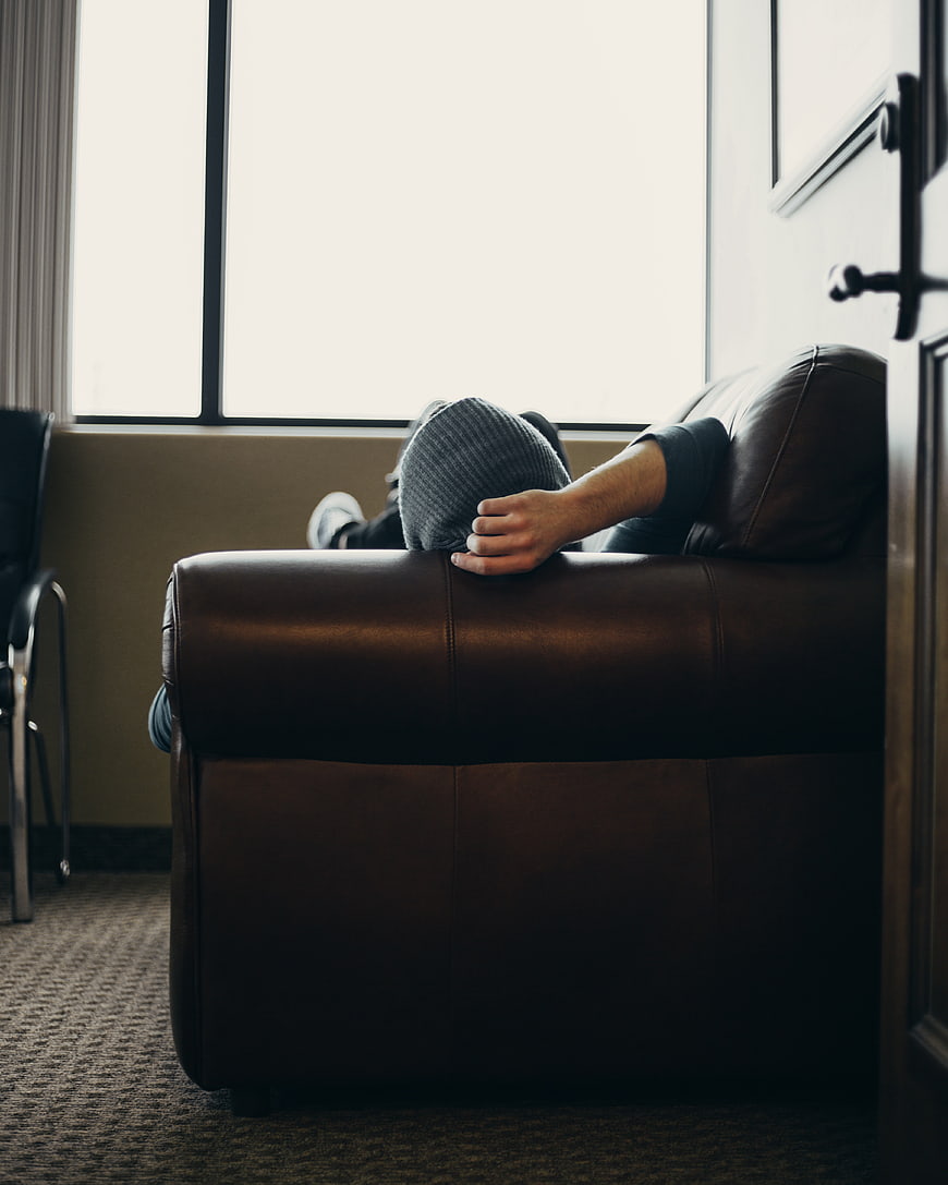 Man resting on leather sofa with head covered by sweater