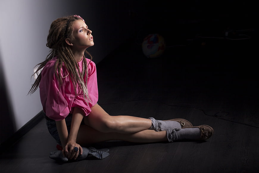 Young woman with dreadlocks sitting on dark studio floor