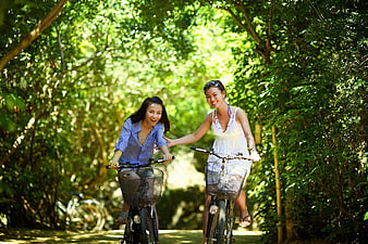 Two Happy Women Cycling Together on a Sunny Forest Path