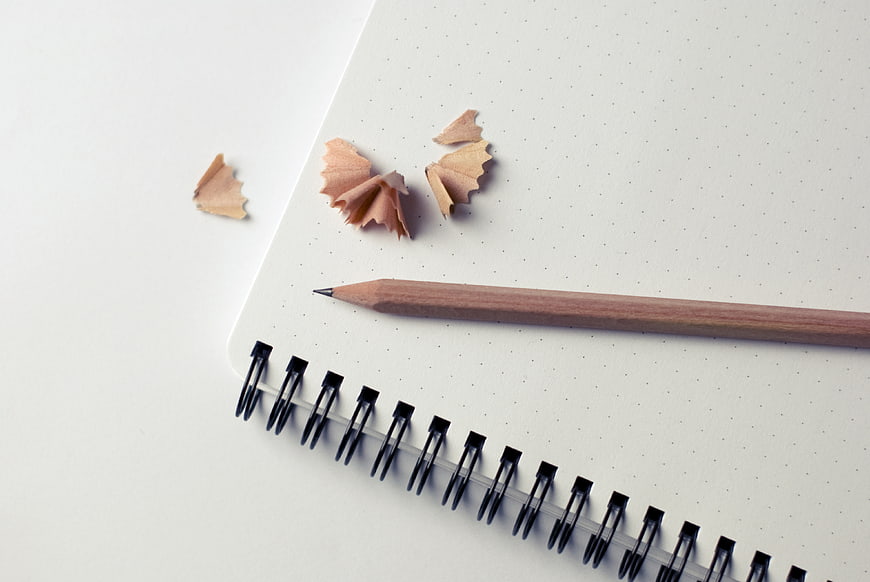 Minimalist wooden pencil and shavings on dotted notebook