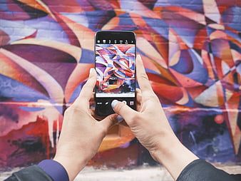 Hands holding smartphone photographing colorful graffiti mural