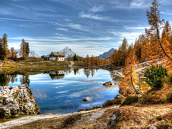 Alpine lake with golden larch trees and mountain hut reflection