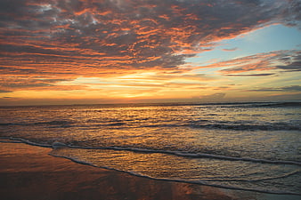 Dramatic Orange Sunset Over Ocean Waves and Sandy Beach