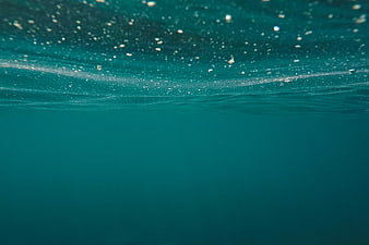 Underwater view of teal ocean surface with bubbles and light