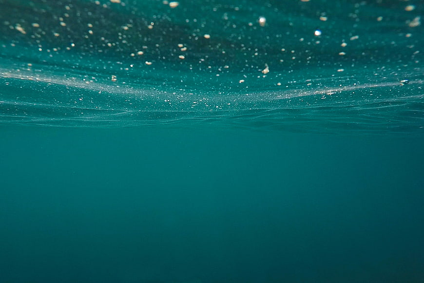 Underwater view of teal ocean surface with bubbles and light
