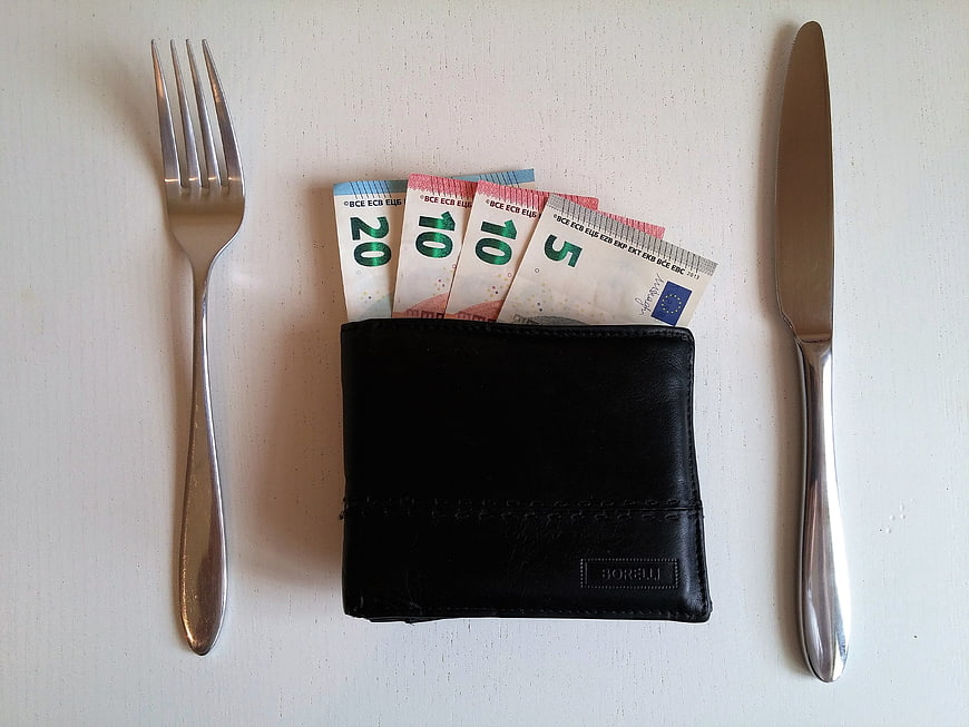 Black wallet with euro banknotes between fork and knife