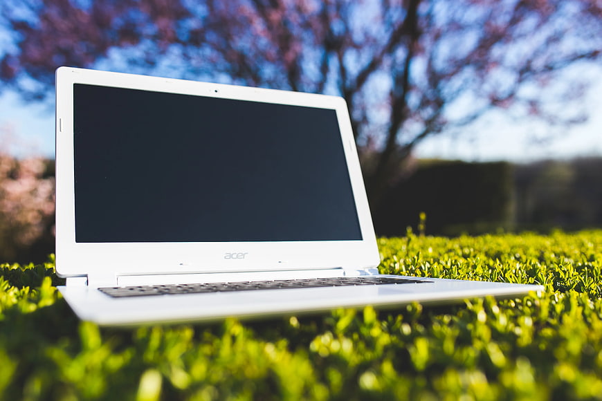 White laptop on green grass with blurred nature background