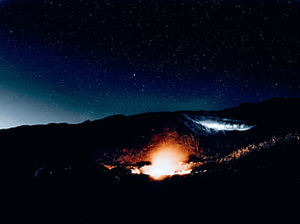 Campfire under starry night sky in mountain landscape