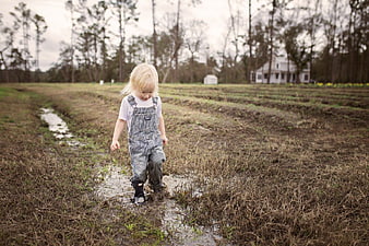 Toddler in overalls splashing in muddy puddle field