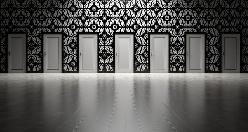 Seven white doors in a room with black and white patterned wallpaper