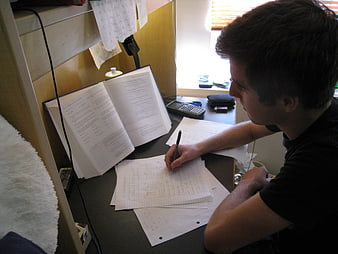 Young man studying at desk with open book and calculator