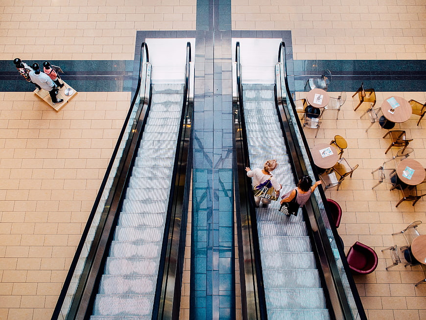 Top-down view of shoppers on escalators in a modern shopping mall atrium