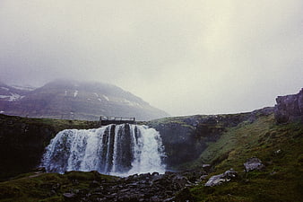 Misty waterfall cascading into rocky pool in green mountain landscape