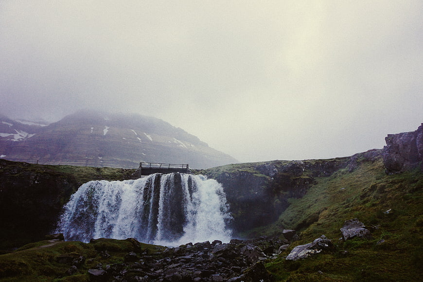 Misty waterfall cascading into rocky pool in green mountain landscape