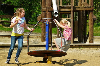 Two young girls playing on a merry-go-round at a sunny playground