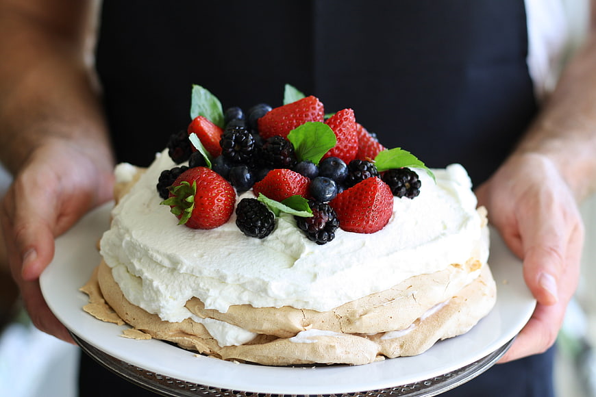 Man holding a fresh berry pavlova cake with whipped cream and mint