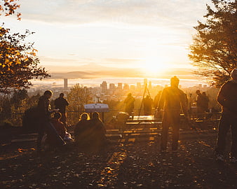 Photographers capturing sunrise over city skyline from hilltop viewpoint