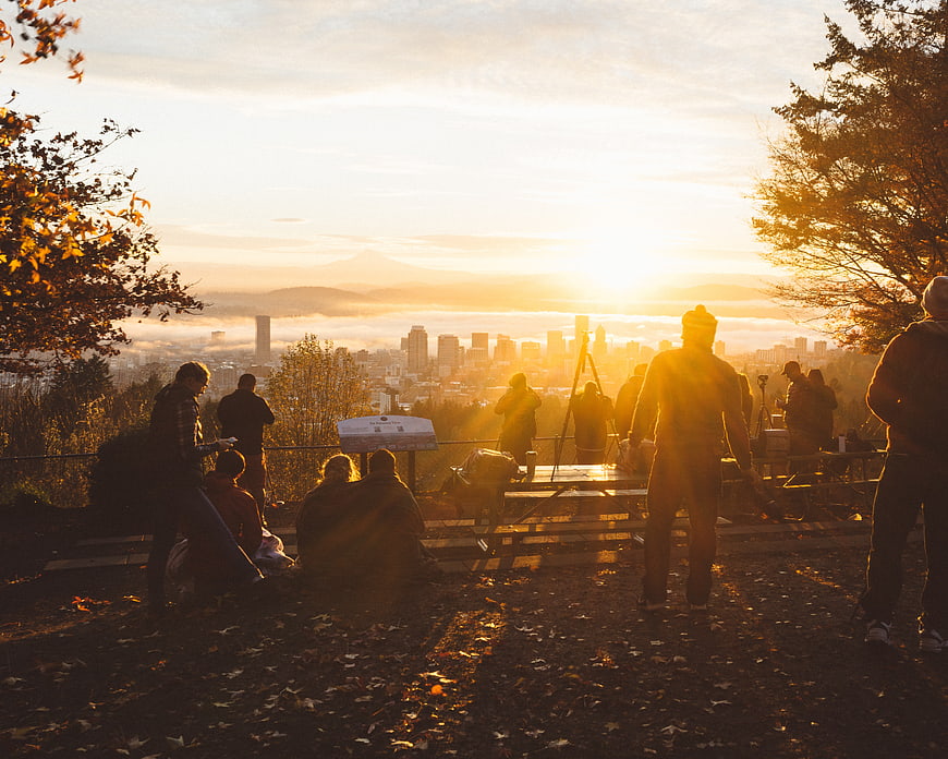 Photographers capturing sunrise over city skyline from hilltop viewpoint