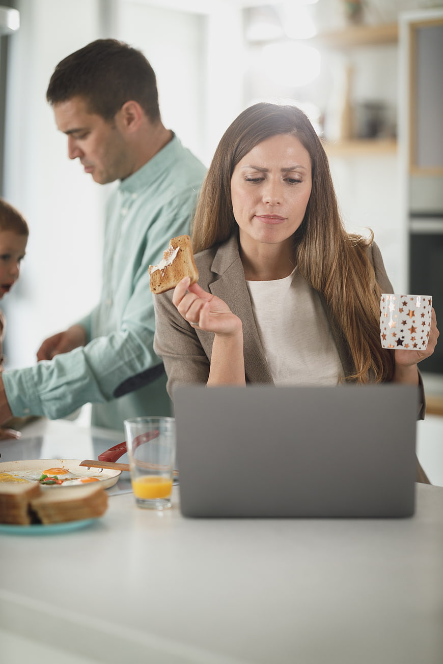 Busy mother working on laptop during family breakfast