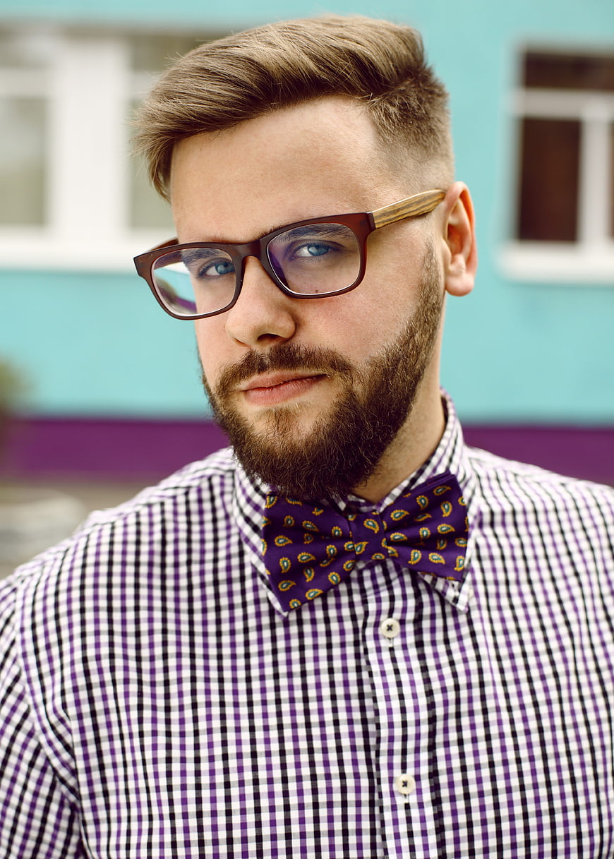 Portrait of a bearded man wearing glasses and a purple paisley bow tie