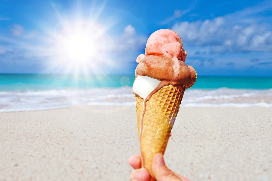 Triple scoop ice cream cone held on a sunny tropical beach