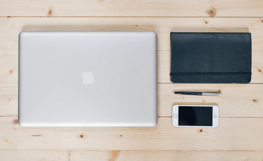 Flat lay of silver laptop, notebook, pen, and smartphone on wood