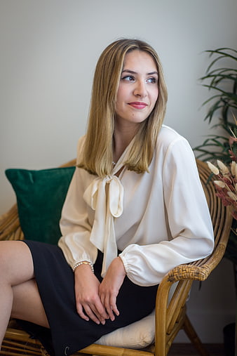 Confident young woman in white blouse sitting in rattan chair