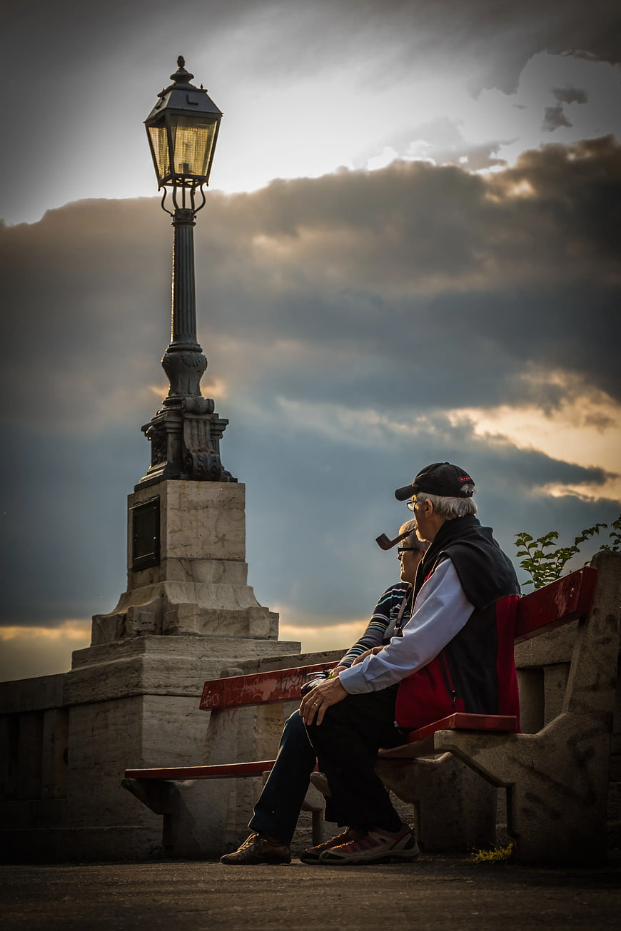Senior Couple Smoking Pipe on Bench at Sunset