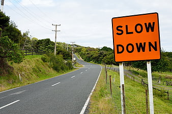 Orange Slow Down Road Sign On Winding Rural Highway