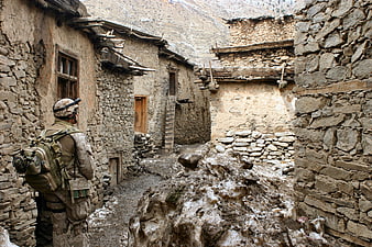 Soldier in camouflage gear walking through stone village alley